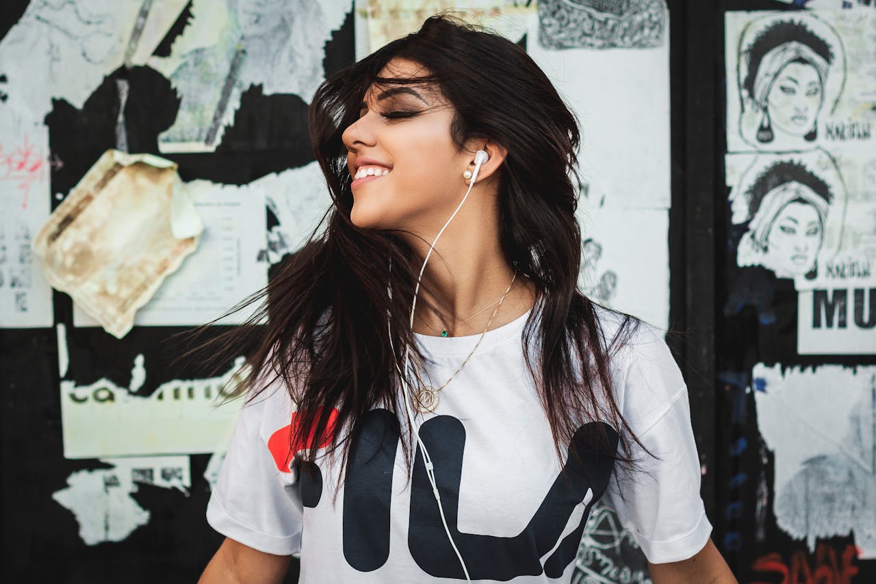 Portrait of a young woman smiling while listening to music with earphones against a graffiti wall.